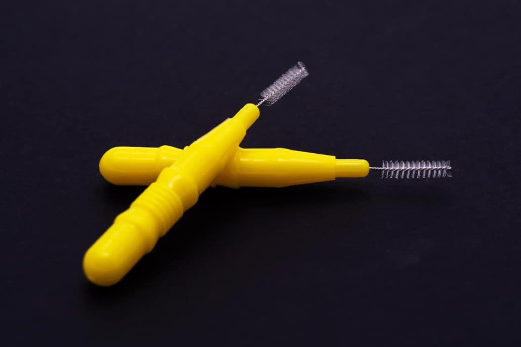 Uma escova interdental de cabo amarelo, ideal para higienizar os espaços entre os dentes, especialmente após procedimentos como a extração do siso.