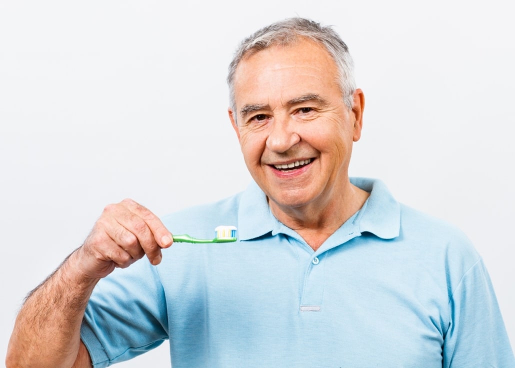 Um homem sênior sorridente, segurando uma escova de dentes, simbolizando a importância da higiene bucal após a colocação de implantes dentários.