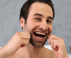 Imagem de um homem sorridente usando fio dental. Ele parece feliz cuidando de sua saúde bucal, destacando a importância do uso regular do fio dental para prevenir problemas como cáries e garantir que nunca mais terá cárie.